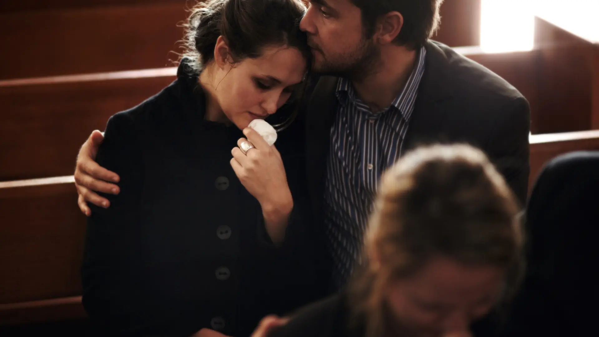 Grieving woman comforted by a man during a memorial service or funeral.