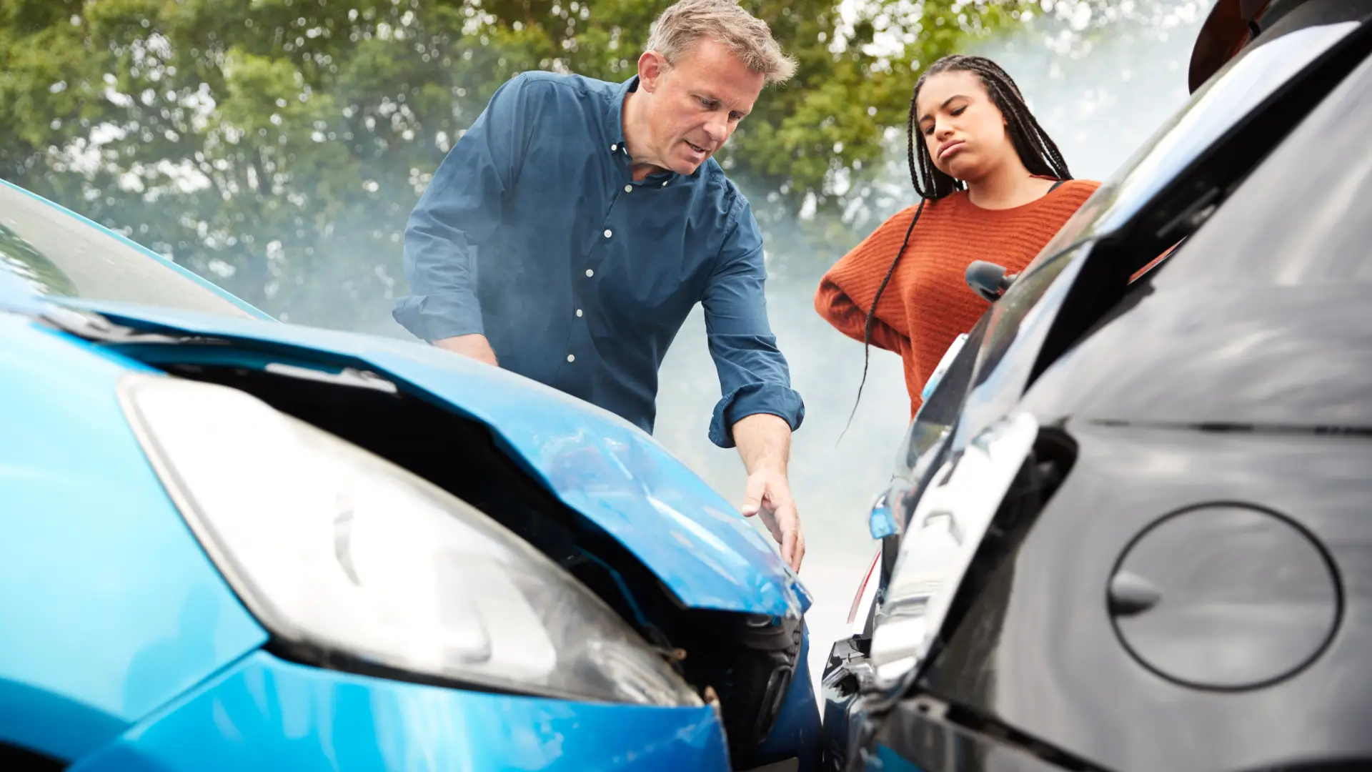 Two people inspecting damage after a car accident involving a blue and a black vehicle.