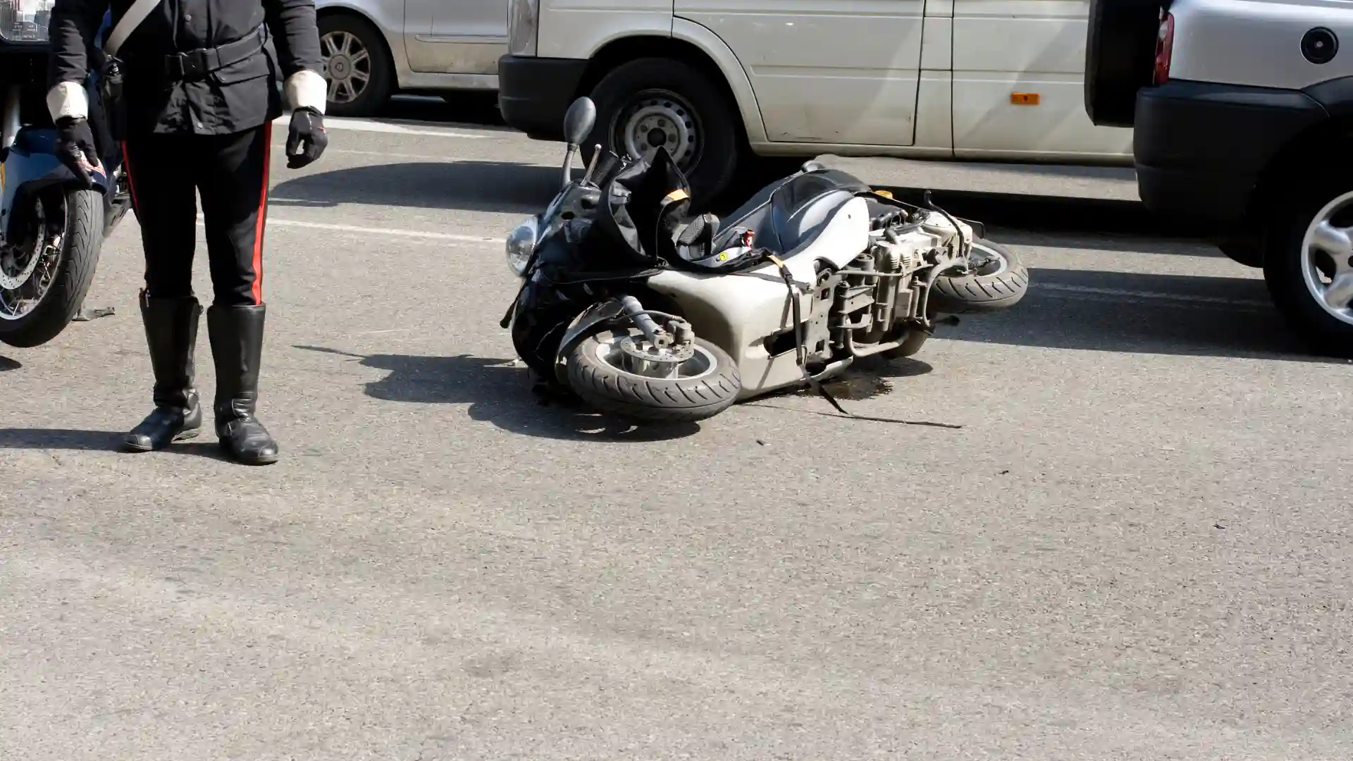 Motorcycle lying on its side on a city street after an accident, with nearby vehicles in the background.